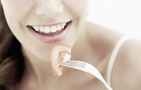 Hình ảnh người phụ nữ đang cầm nĩa với một miếng cà chua ở trên